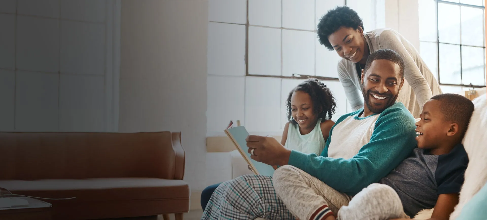 A family sitting together on the sofa, smiling as they look at their book